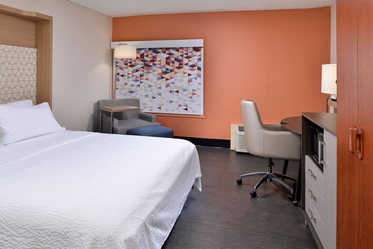 Una habitación de hotel con una cama grande, un escritorio, una silla y una lámpara fijada a la pared.
