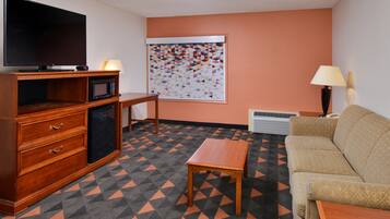 A compact living room with a sofa, a television, a microwave, a small table, and a patterned rug.