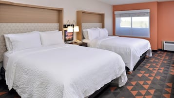 Een hotelkamer met twee bedden, een nachtkastje met een lamp, een raam met jaloezieën en een kamer met een patroon vloer.