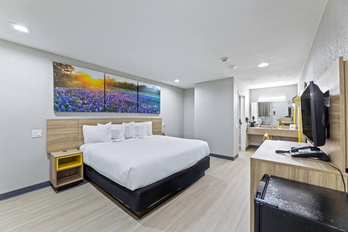 A modern hotel room with a large bed, a desk with a computer, and a bathroom with a mirror.