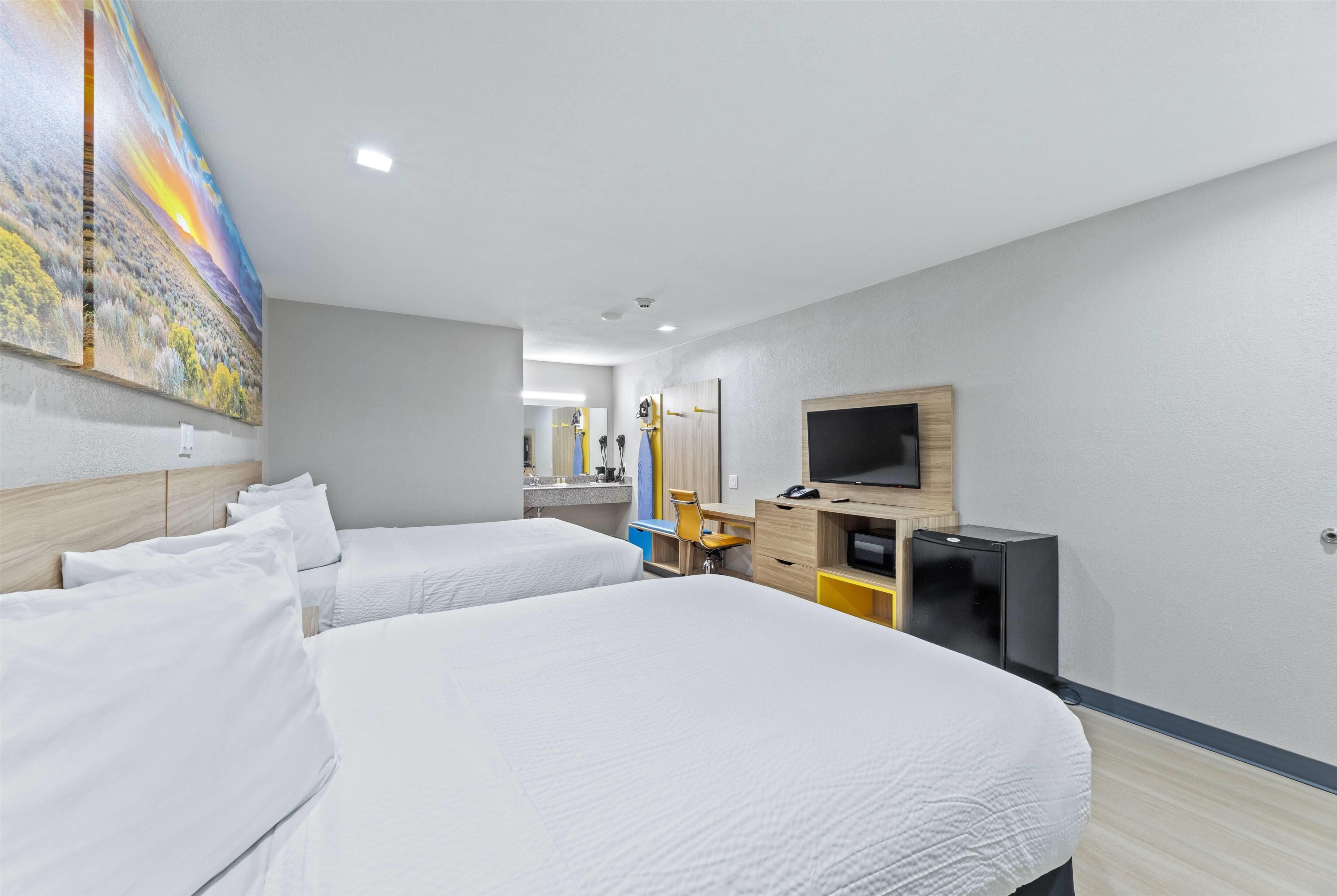 Une chambre d’hôtel avec deux lits, un bureau avec une chaise, une télévision et un petit réfrigérateur.