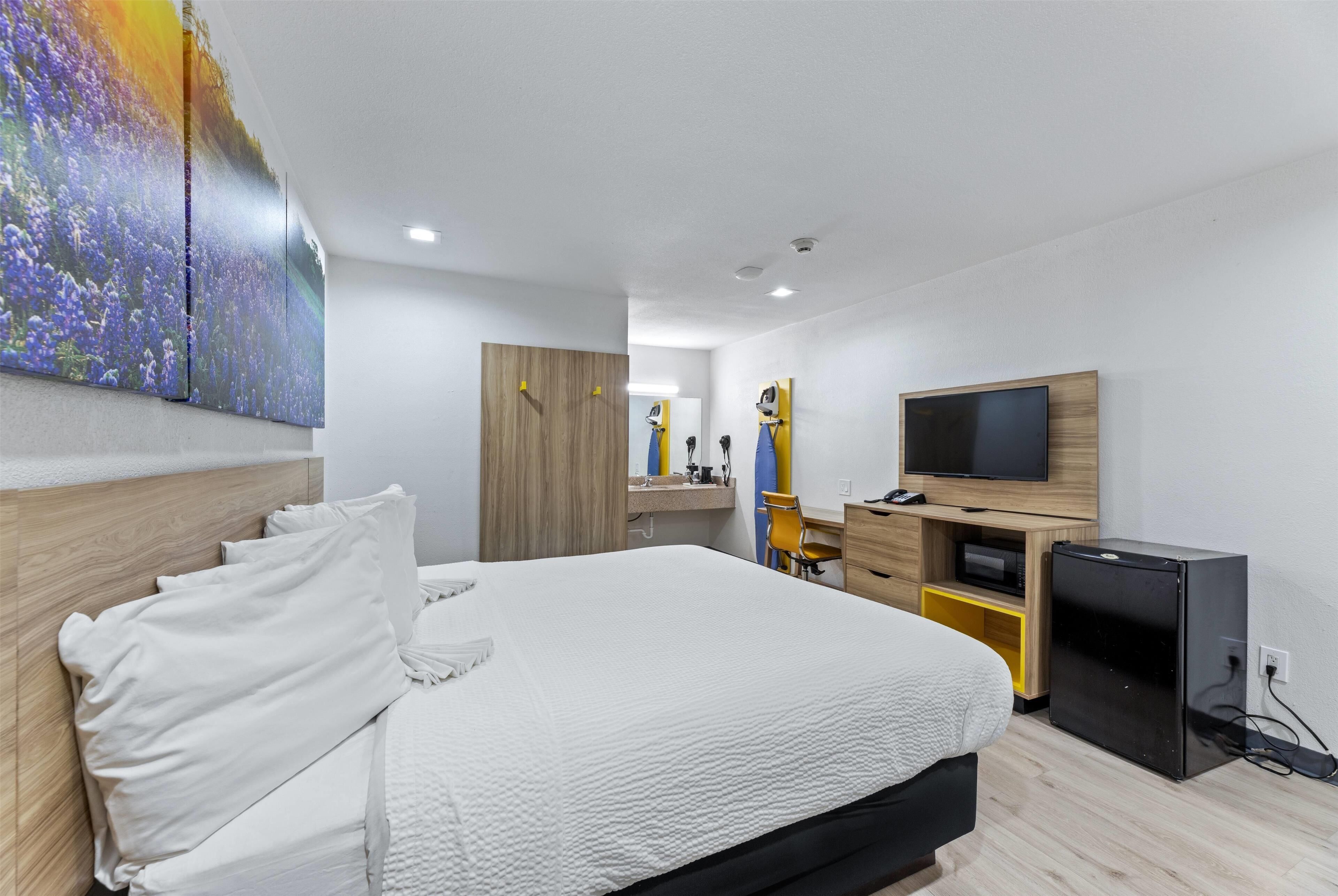 Une chambre d’hôtel moderne équipée d’un grand lit, d’une télévision, d’un petit réfrigérateur et d’un bureau avec une chaise.