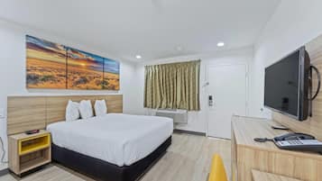 A hotel room with a bed, a desk with a phone, a TV, and a painting of a sunset on the wall.