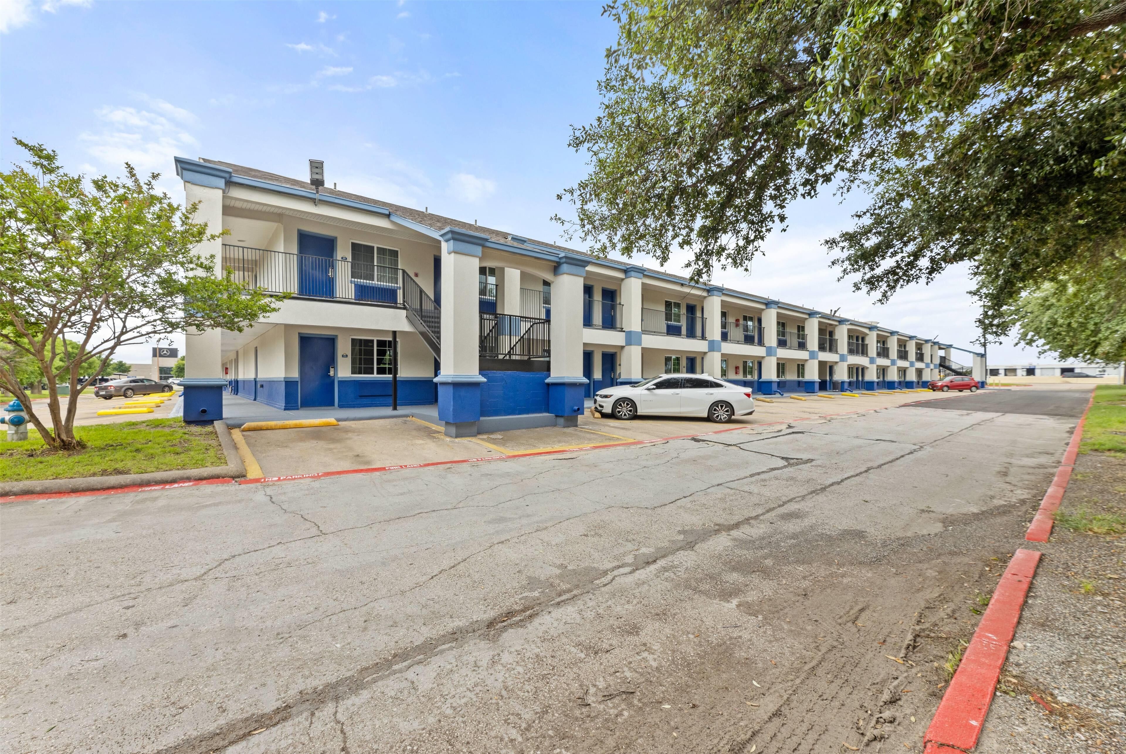 A multi-story motel with a blue and white exterior, a parking lot, and a tree in the foreground.