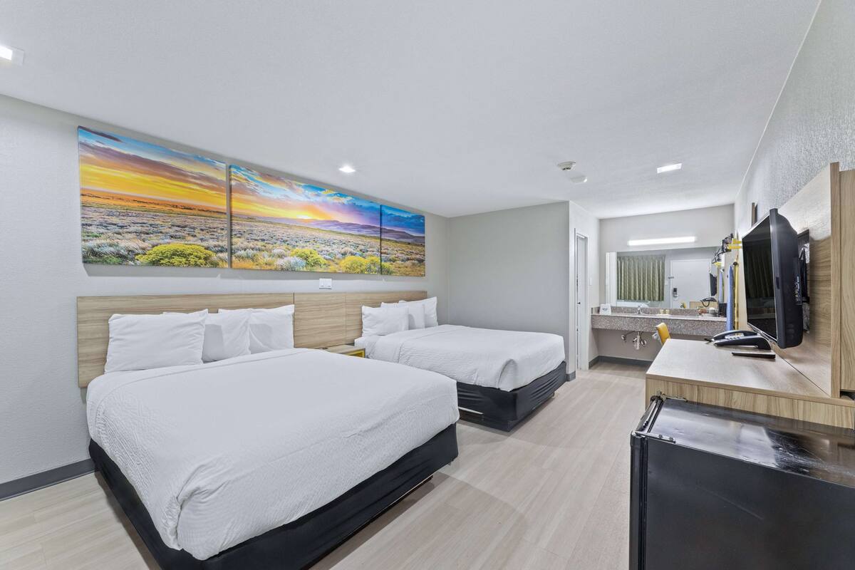 A hotel room with two beds, a large painting of a landscape, a desk with a computer, and a mirror.