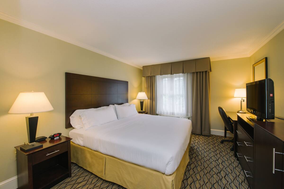 A hotel room with a large bed, two bedside tables with lamps, a desk with a television, and a window with curtains.