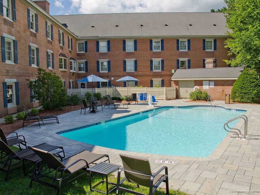A brick building with a swimming pool, lounge chairs, and umbrellas.