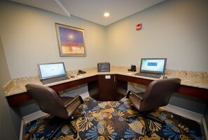 A conference room with two desks, each with a laptop and a telephone. There are two chairs in front of the desks, and a carpeted floor. A painting hangs on the wall above the desks. - Holiday Inn Express & Suites Merrimack – Nashua by IHG (Merrimack)