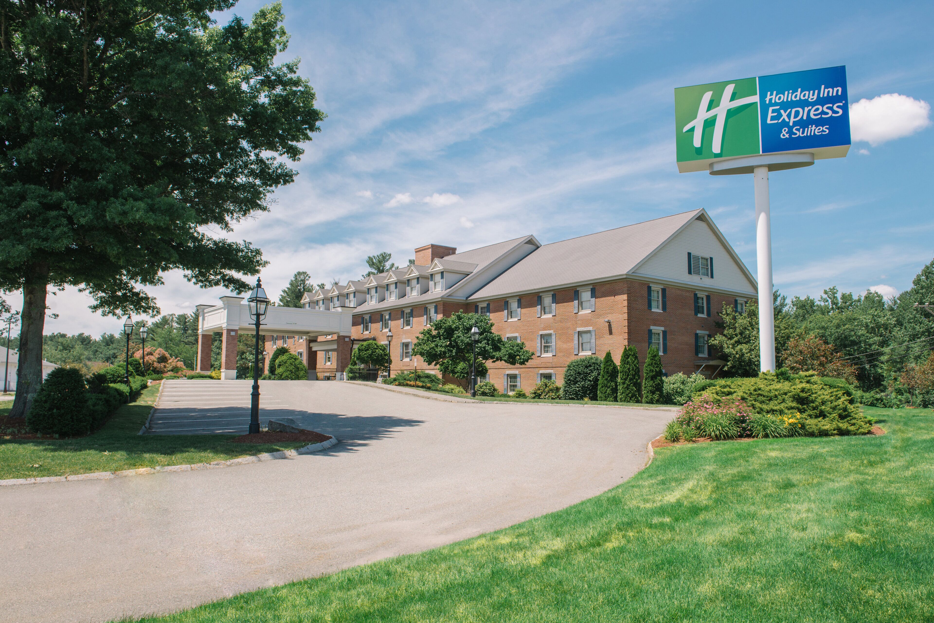 A Holiday Inn Express & Suites hotel with a brick facade, a covered parking area, and a well-maintained lawn.