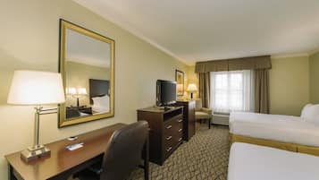 A hotel room with a bed, a desk with a chair, a television, a mirror, and a window with curtains.
