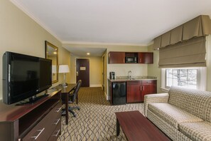 A hotel room with a TV, desk, chair, sofa, kitchenette, and a bathroom door. - Holiday Inn Express & Suites Merrimack – Nashua by IHG (Merrimack)