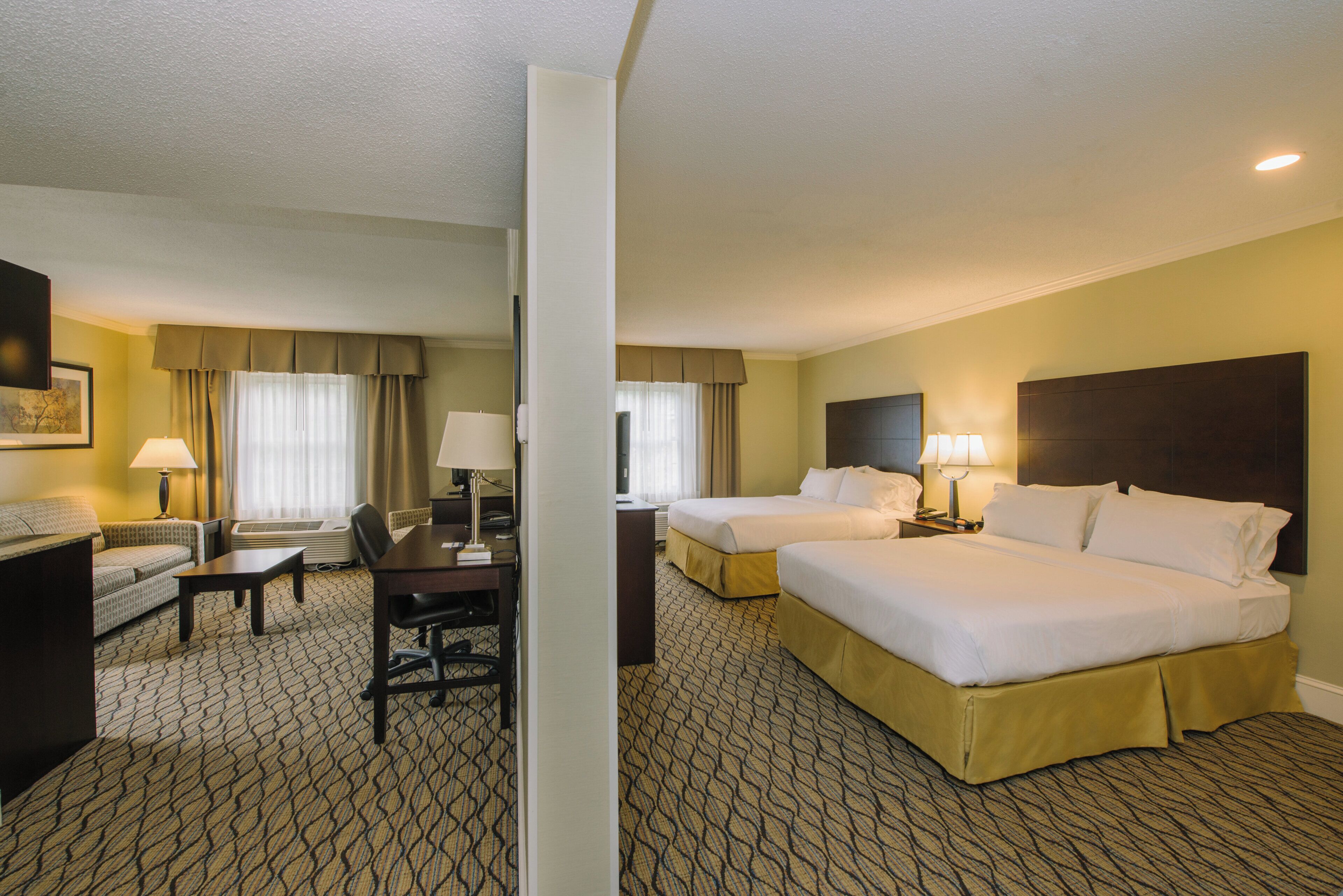 A hotel room with two beds, a desk, a chair, and a television.