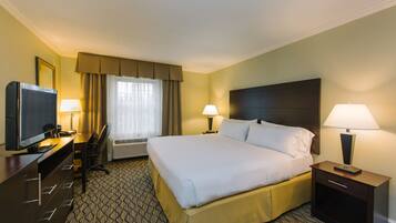 A hotel room with a large bed, a desk with a TV, two bedside lamps, and a window with curtains.