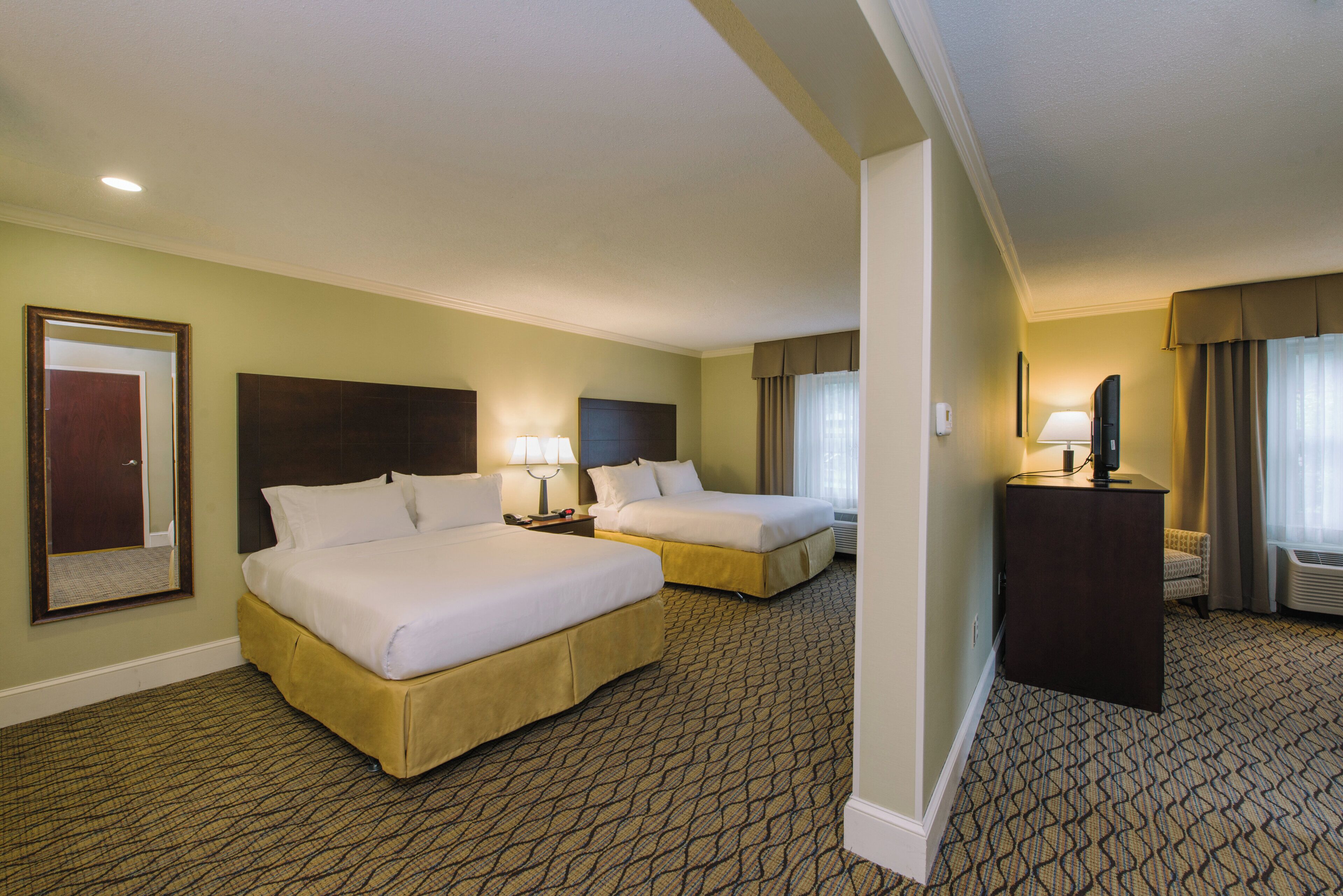 A hotel room with two beds, a desk, a television, and a mirror.