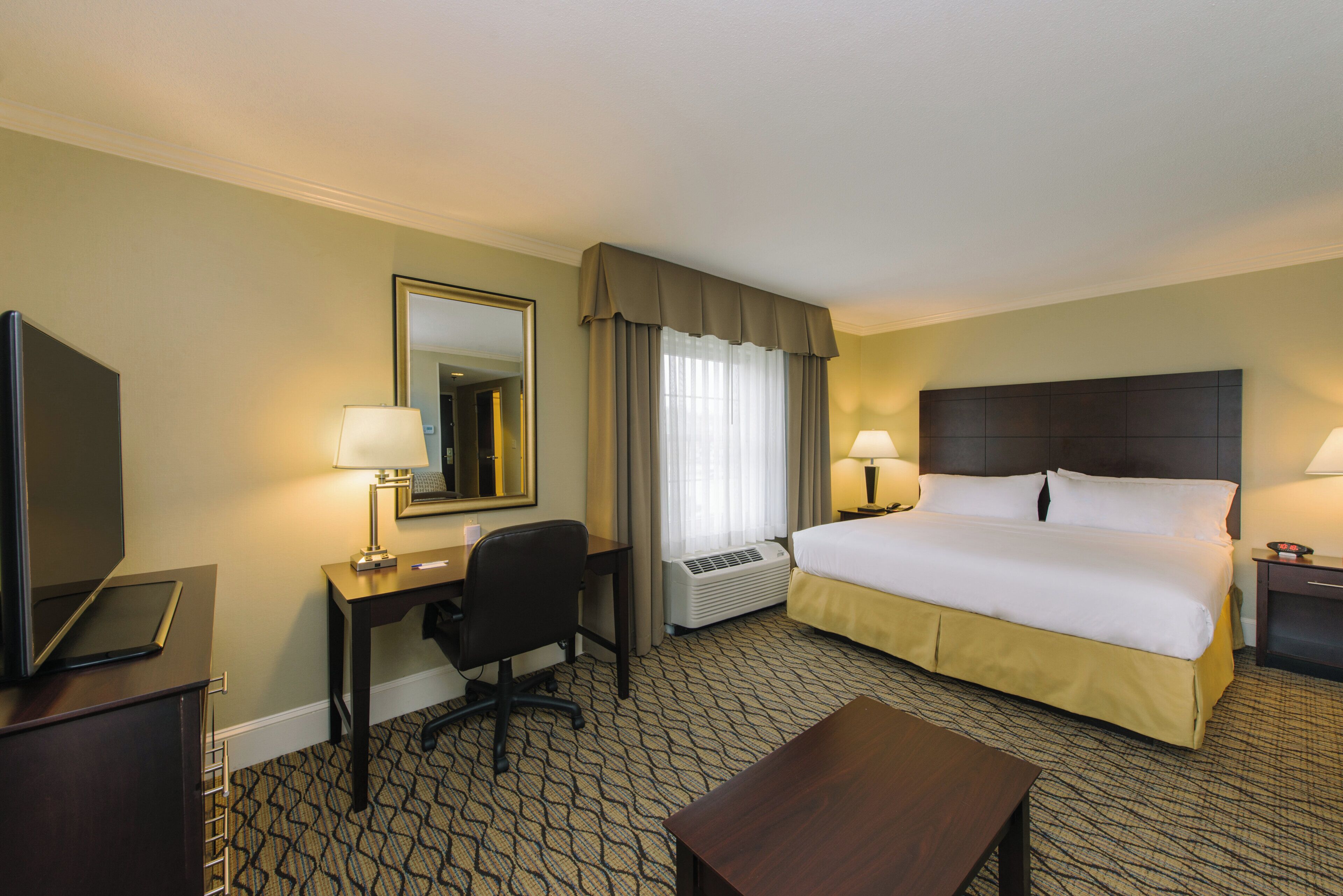 A hotel room with a bed, desk, chair, television, and a large mirror.