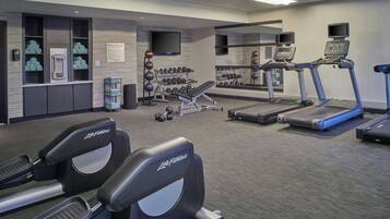 A gym with treadmills, a bench, dumbbells, and a water dispenser.