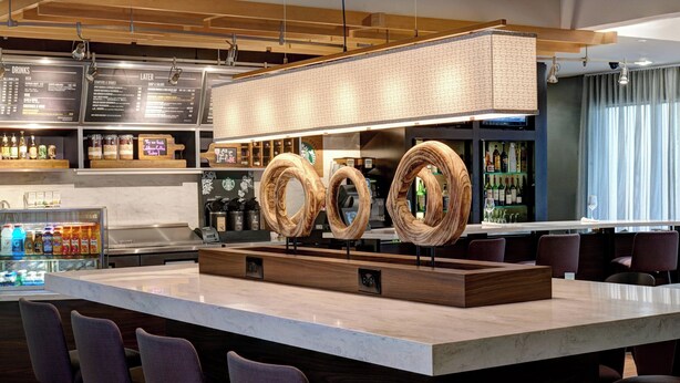 A modern bar area with a central island, bar stools, and a menu board above. - Courtyard by Marriott Chicago Oakbrook Terrace (Villa Park)