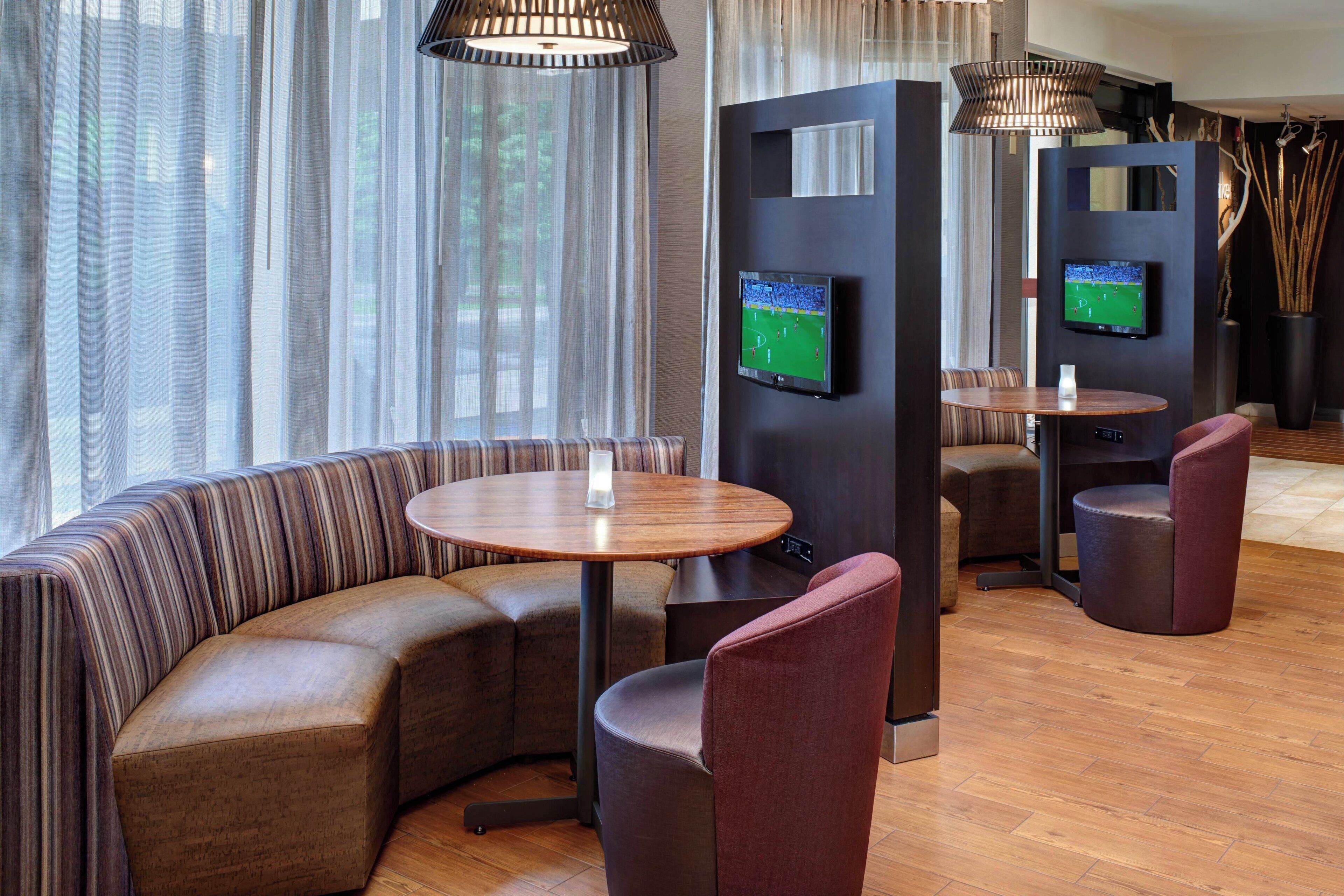 A modern hotel lobby with a curved seating area, two televisions mounted on a wall, and a wooden floor.