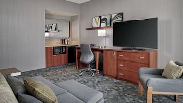 A hotel room with a sofa, a desk with a chair, a television, and a small kitchenette.