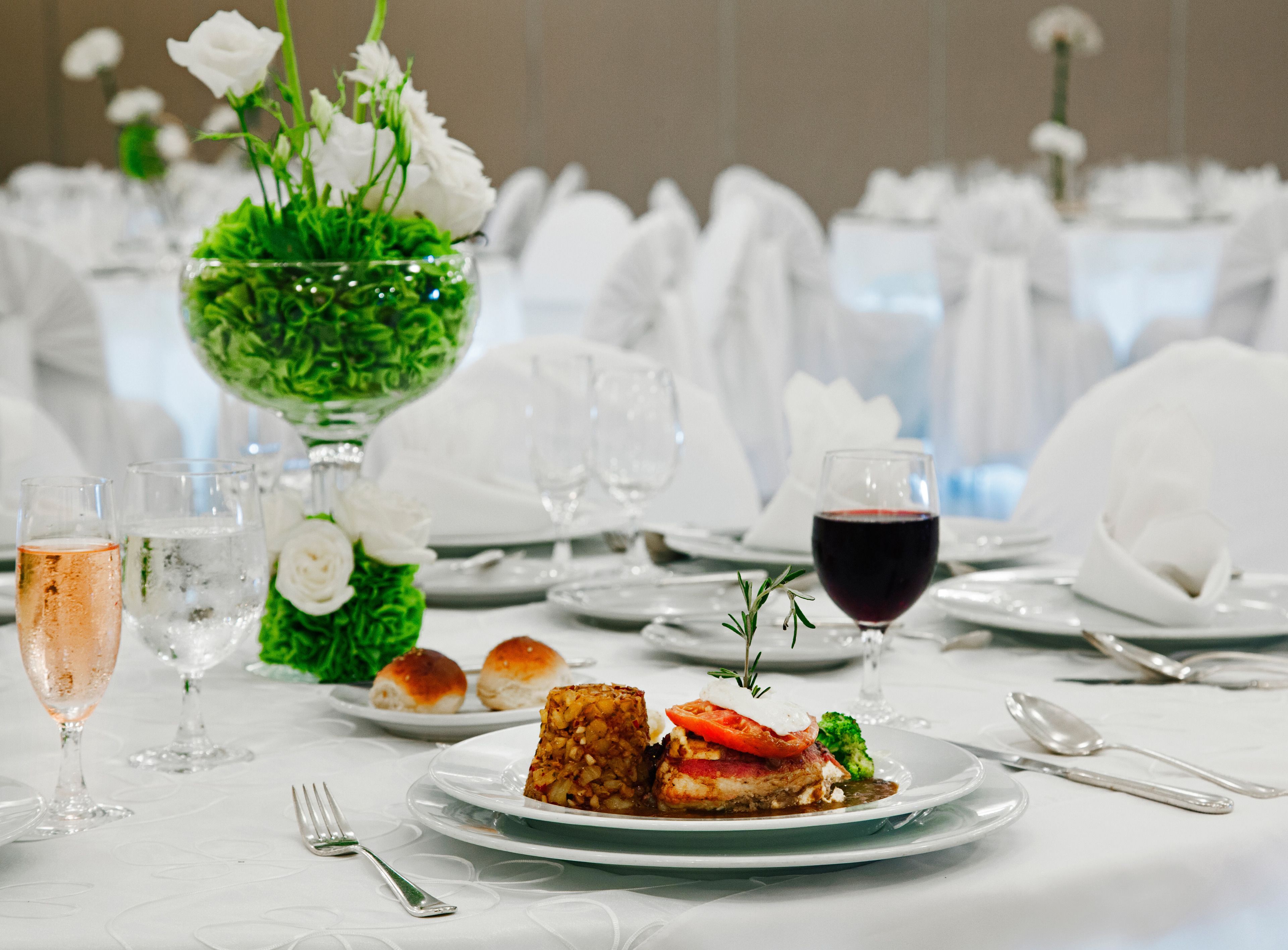 Une table à manger élégante, recouverte d’une nappe blanche, agrémentée de verres et d’un centre de table composé de fleurs blanches.