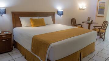 A hotel room with a large bed, two bedside lamps, a small table with chairs, and a framed picture on the wall.