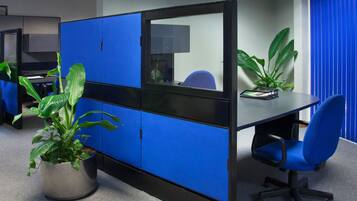 A modern office cubicle with blue partitions, a desk, and a chair. There is a potted plant on the floor.