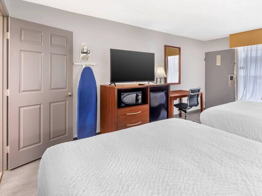 A hotel room with two beds, a desk with a TV, a microwave, a chair, and a door.