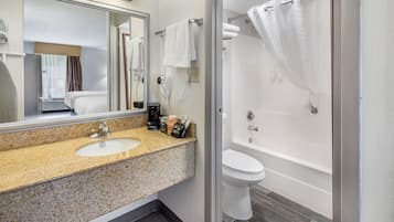 A hotel bathroom with a granite countertop sink, a mirror, a white toilet, and a bathtub with a shower curtain.