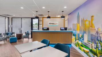 A hotel reception area with a cityscape mural, modern furniture, and a wooden reception desk.