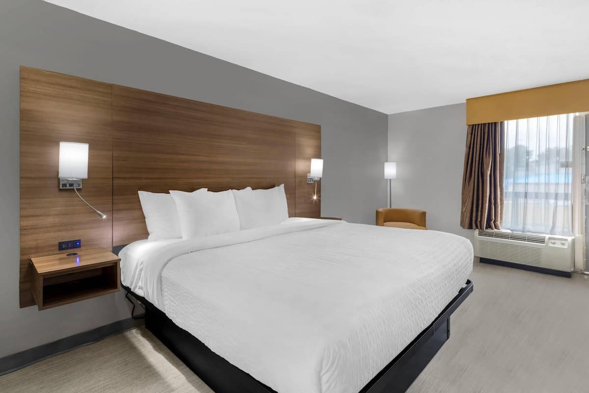 Una habitación de hotel moderna con una cama grande, mesitas de noche, luces fijadas a la pared y un ventanal con cortinas.