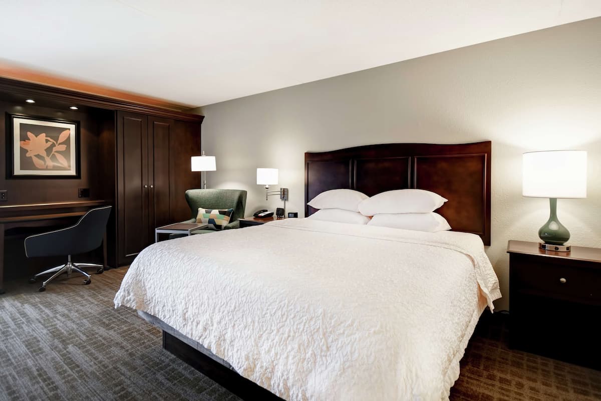 Una habitación de hotel con una cama grande, un escritorio, una silla y una mesita de noche con lámpara.