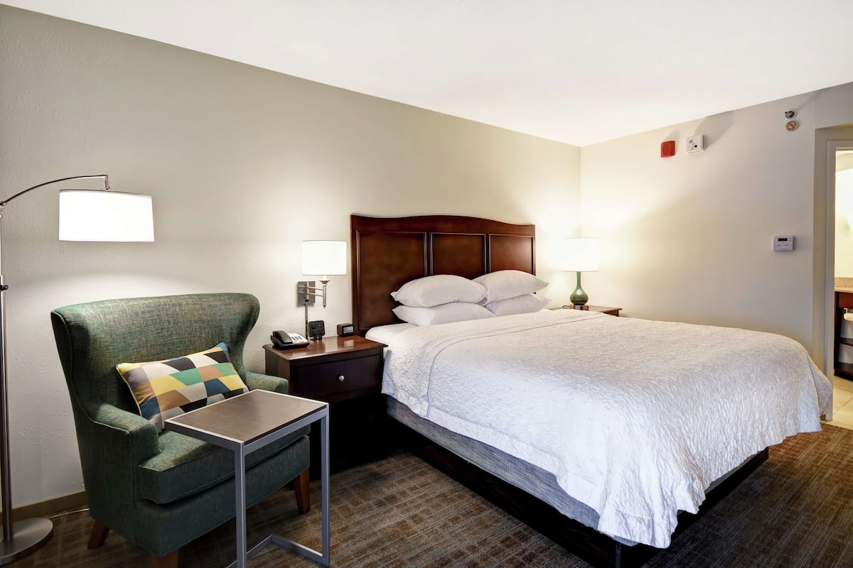 Una habitación de hotel con una cama, una silla, una mesita de noche, una lámpara y una pequeña mesa.
