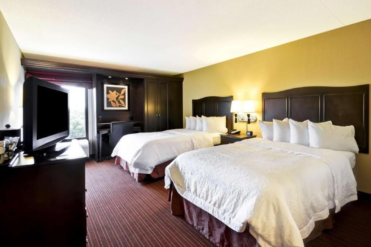 A hotel room with two beds, a television, a desk, and a window.