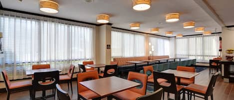 A restaurant with multiple tables and booths, large windows with blinds, and ceiling lights.