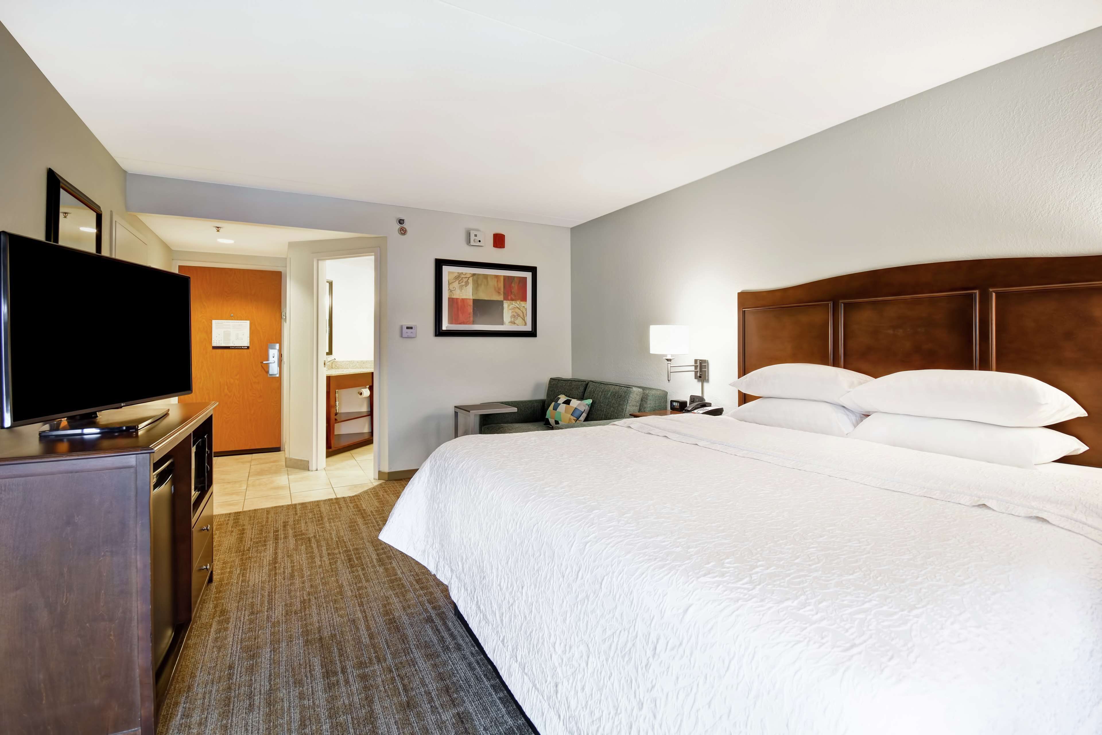 A hotel room with a large bed, a flat-screen TV, a desk, and a chair.