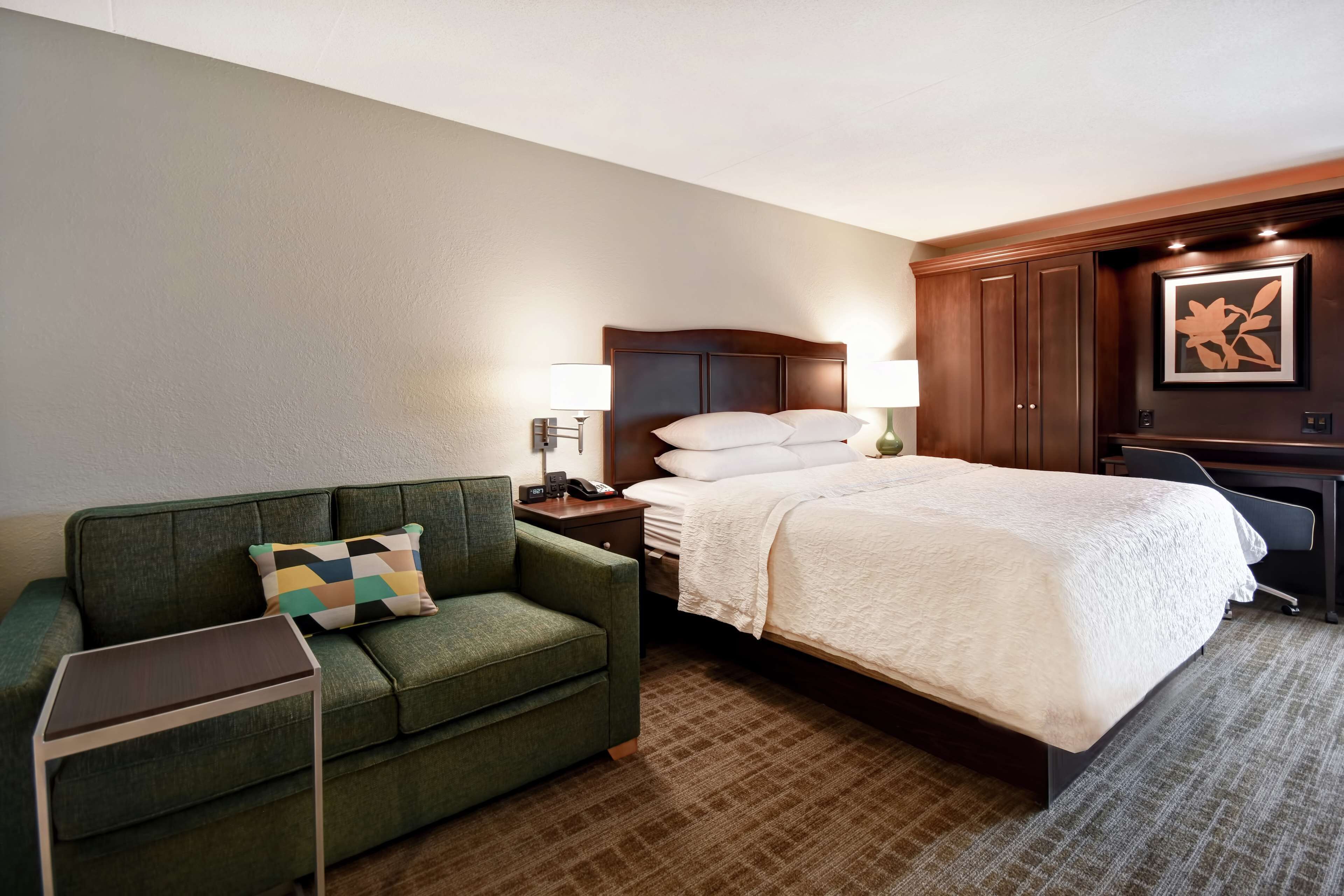 Une chambre d’hôtel avec un lit, un canapé vert, un bureau et une table de chevet.