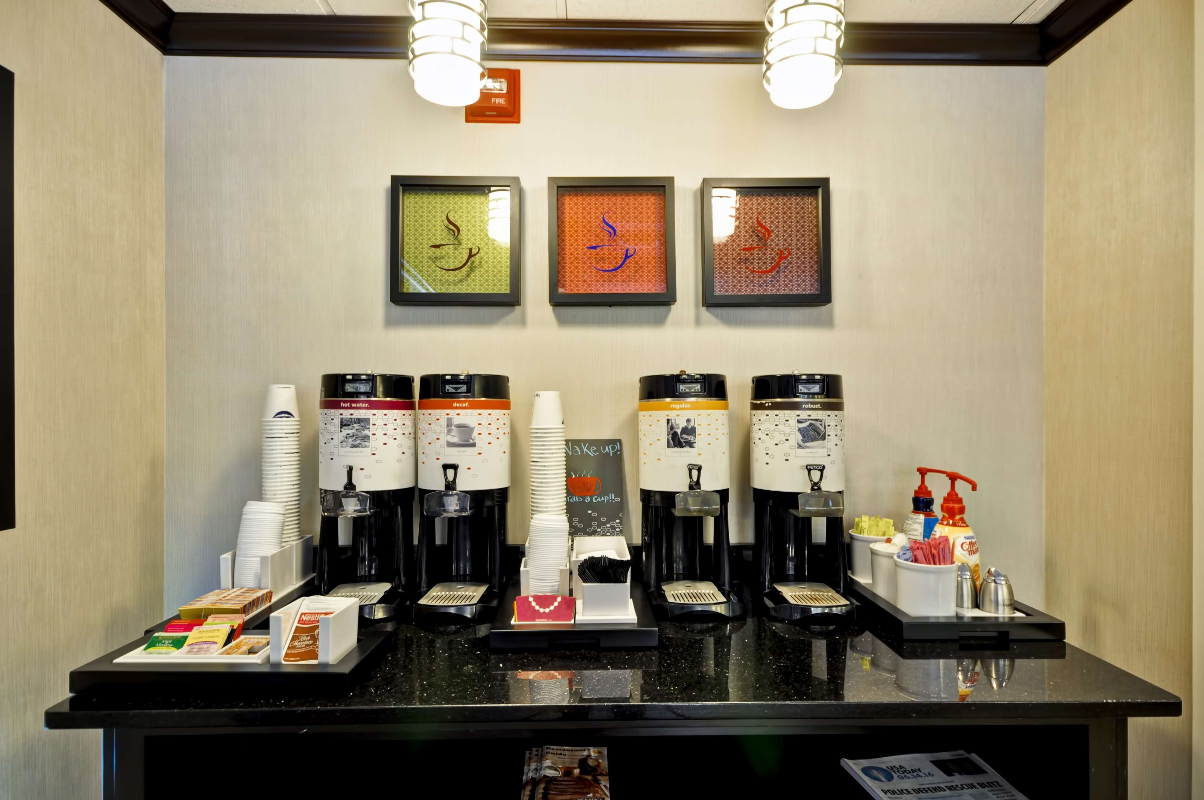 Una estación de café con varias cafeteras, vasos desechables y condimentos.