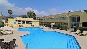 A swimming pool with lounge chairs and umbrellas, surrounded by a building with multiple windows and a clear sky. - Holiday Inn Monterrey Norte by IHG (San Nicolas de los Garza)