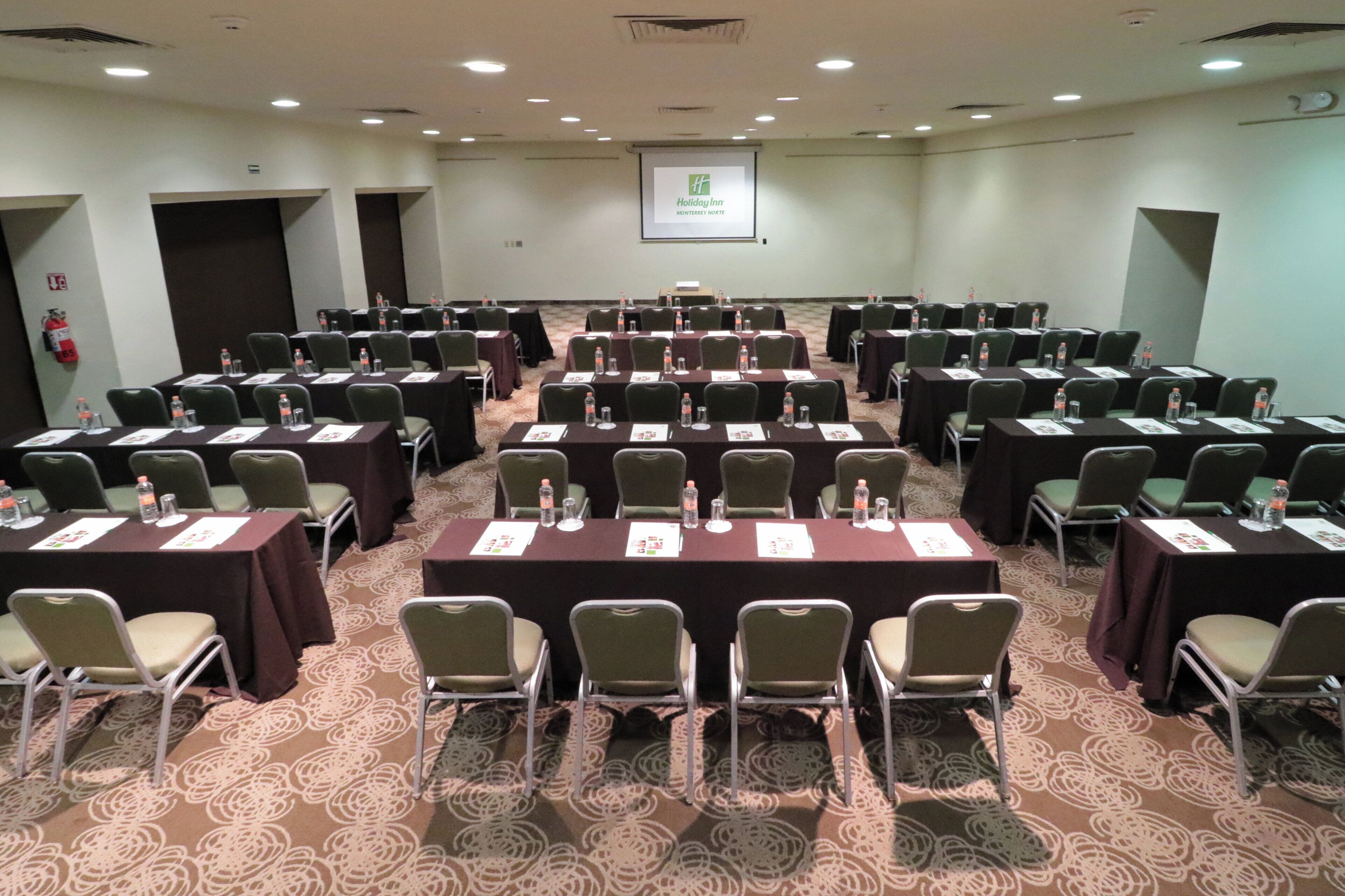 Un salón de conferencias con filas de mesas y sillas, equipado con tarjetas de identificación y botellas de agua.
