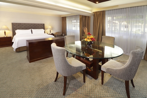 A hotel room with a bed, a glass table with chairs, a nightstand, and a lamp.