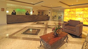 A hotel lobby with a reception desk, a seating area with a sofa and a coffee table, and a decorative wall. - Holiday Inn Monterrey Norte by IHG (San Nicolas de los Garza)