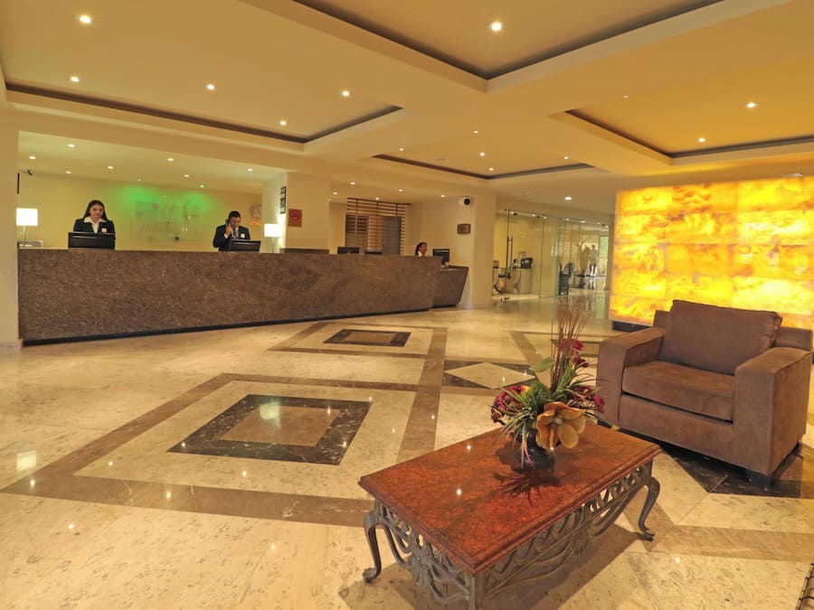 A hotel lobby with a reception desk, a seating area with a sofa and a coffee table, and a decorative wall.