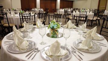 A banquet hall with round tables set for dining, featuring white tablecloths and silverware.