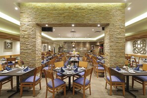 A dining area with stone walls, multiple tables, and chairs. - Holiday Inn Monterrey Norte by IHG (San Nicolas de los Garza)