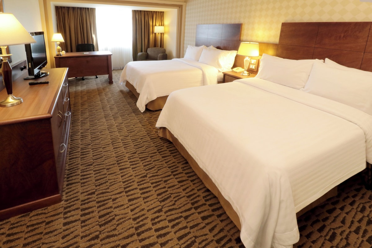 A hotel room with two beds, a desk, a chair, and a television.