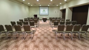 A conference room with rows of chairs, a podium, and a projection screen displaying a logo. - Holiday Inn Monterrey Norte by IHG (San Nicolas de los Garza)