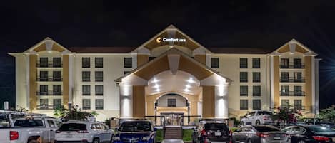 A Comfort Inn hotel with a central entrance, multiple parking spaces, and a well-lit facade.