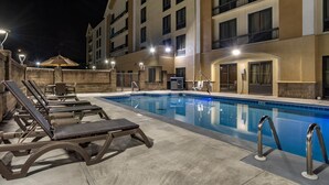 A swimming pool with lounge chairs and a covered seating area, surrounded by a multi-story building with balconies.