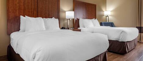 A hotel room with two beds, wooden headboards, bedside tables with lamps, and a blue chair.