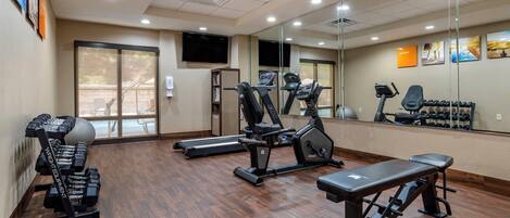 Een sportschool met trainingsapparatuur, een bank en een spiegelwand.